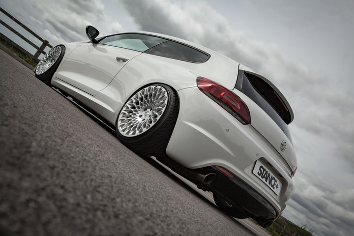 White VW Scirocco car  distinctive Cast13 RB2 wheels on a road under a cloudy sky.  Fitted with Stance+ Street Coilover Suspension.